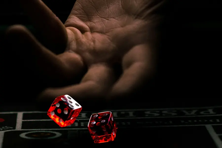 A hand rolling two red dice across a casino table